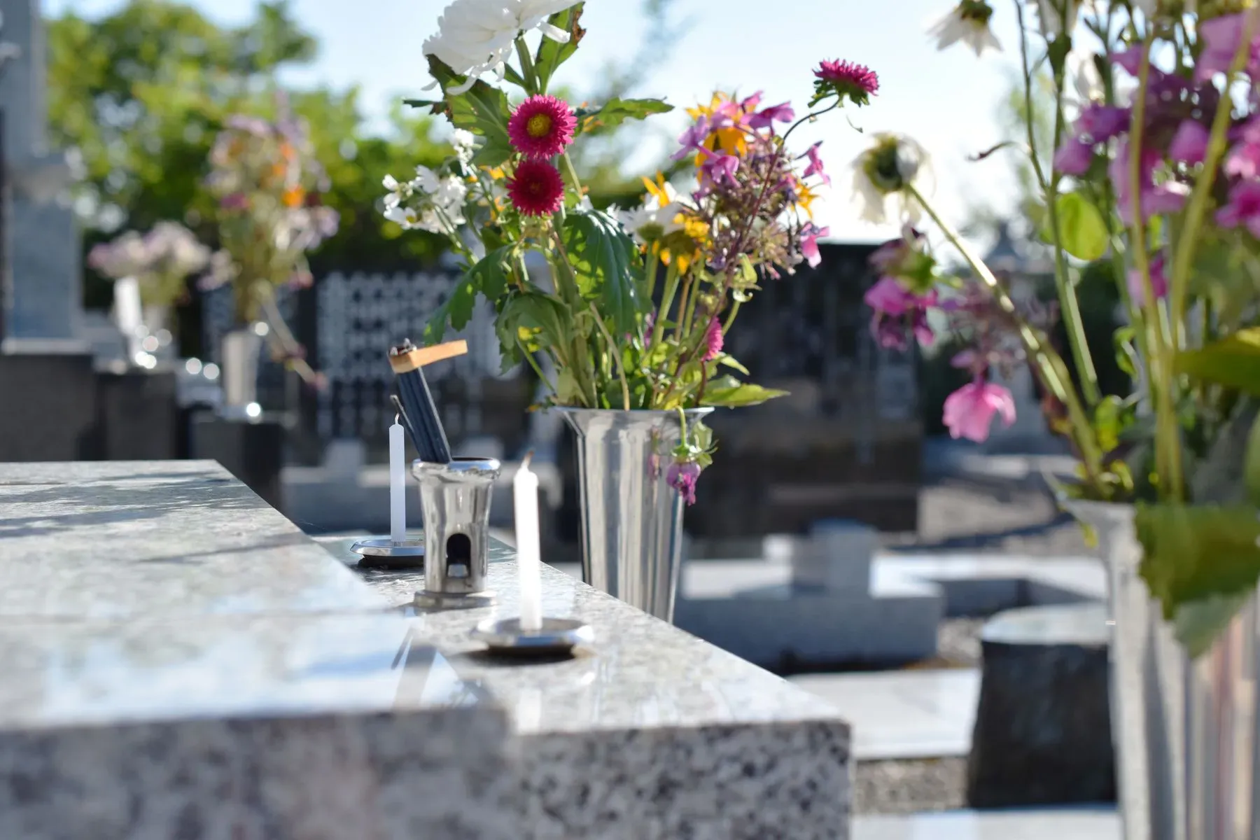 Vases de fleurs et bougies déposés sur une tombe en marbre au cimetière.